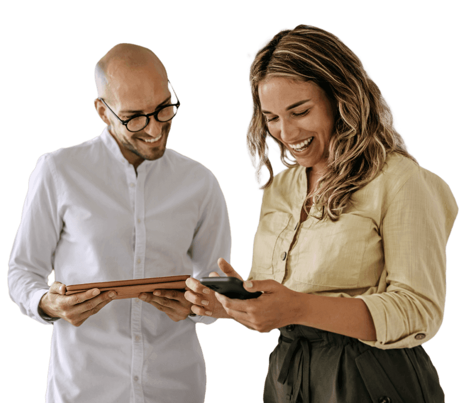 A man and woman standing next to each other looking at a tablet and phone while smiling.